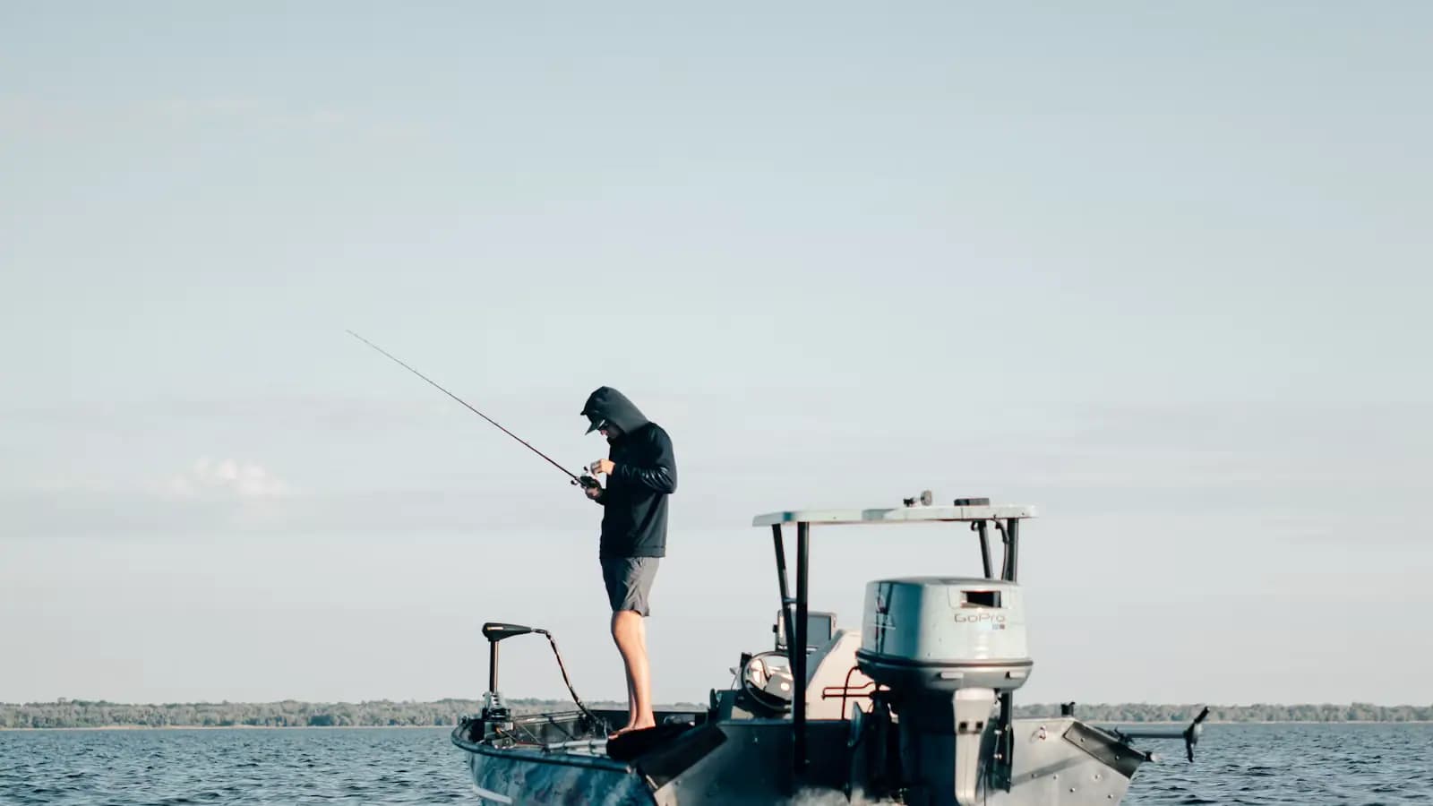 An angler standing on the bow platform of a shallow-draft boat casting across open water